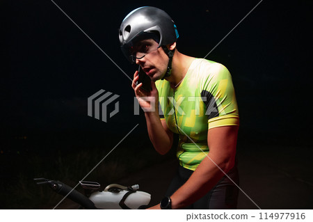 A triathlete using a smartphone while taking a break from a hard night's cycling training 114977916
