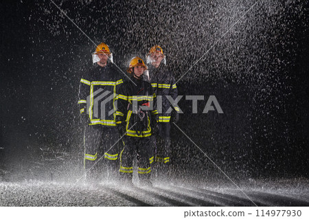 A group of professional firefighters marching through the rainy night on a rescue mission, their determined strides and fearless expressions reflecting their unwavering bravery and unwavering 114977930