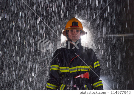 A determined female firefighter in a professional uniform striding through the dangerous, rainy night on a daring rescue mission, showcasing her unwavering bravery and commitment to saving lives. A determined female firefighter in a professional uniform striding through the dangerous, rainy night on a daring rescue mission, showcasing her unwavering bravery and commitment to saving lives. 114977943