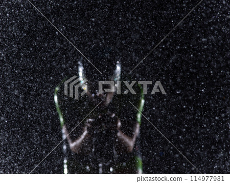 A triathlete braving the rain as he cycles through the night, preparing himself for the upcoming marathon. The blurred raindrops in the foreground and the dark, moody atmosphere in the background add 114977981