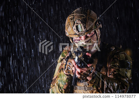 Army soldier in Combat Uniforms with an assault rifle, plate carrier and combat helmet going on a dangerous mission on a rainy night. 114978077
