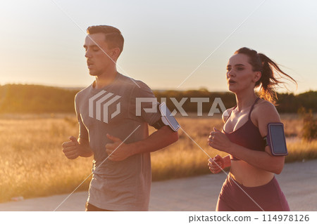 A handsome young couple running together during the early morning hours, with the mesmerizing sunrise casting a warm glow, symbolizing their shared love and vitality A handsome young couple running together during the early morning hours, with the mesmerizing sunrise casting a warm glow, symbolizing their shared love and vitality 114978126