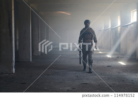 A professional soldier in an abandoned building shows courage and determination in a war campaign 114978152