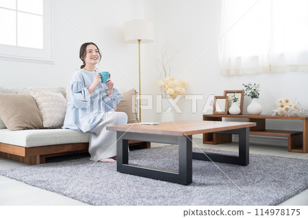 A woman relaxing in the living room with a cup of coffee or a drink 114978175