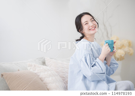Woman relaxing in the living room with coffee or drink, close-up looking at camera Woman relaxing in the living room with coffee or drink, close-up looking at camera 114978193