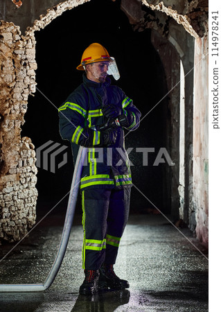 Firefighter using a water hose to eliminate a fire hazard. Team of female and male firemen in dangerous rescue mission.  114978241