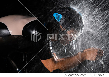 A triathlete braving the rain as he cycles through the night, preparing himself for the upcoming marathon. The blurred raindrops in the foreground and the dark, moody atmosphere in the background add 114978246