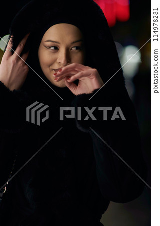 Muslim woman walking on an urban city street on a cold winter night wearing hijab Muslim woman walking on an urban city street on a cold winter night wearing hijab 114978281