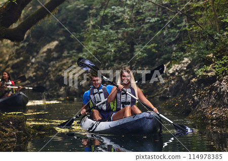 A group of friends enjoying having fun and kayaking while exploring the calm river, surrounding forest and large natural river canyons A group of friends enjoying having fun and kayaking while exploring the calm river, surrounding forest and large natural river canyons 114978385