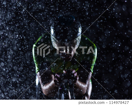 A triathlete braving the rain as he cycles through the night, preparing himself for the upcoming marathon. The blurred raindrops in the foreground and the dark, moody atmosphere in the background add 114978427