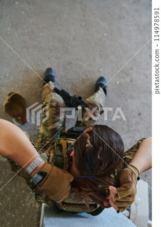 A woman in a professional military uniform sits in an abandoned building, ready for a dangerous mission, exuding bravery and determination 114978591