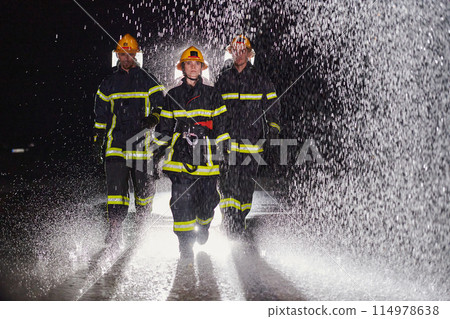 A group of professional firefighters marching through the rainy night on a rescue mission, their determined strides and fearless expressions reflecting their unwavering bravery and unwavering A group of professional firefighters marching through the rainy night on a rescue mission, their determined strides and fearless expressions reflecting their unwavering bravery and unwavering 114978638