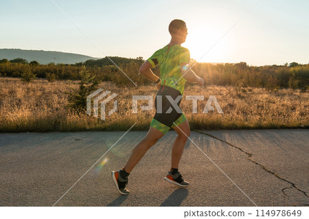 Triathlete in professional gear running early in the morning, preparing for a marathon, dedication to sport and readiness to take on the challenges of a marathon. Triathlete in professional gear running early in the morning, preparing for a marathon, dedication to sport and readiness to take on the challenges of a marathon. 114978649