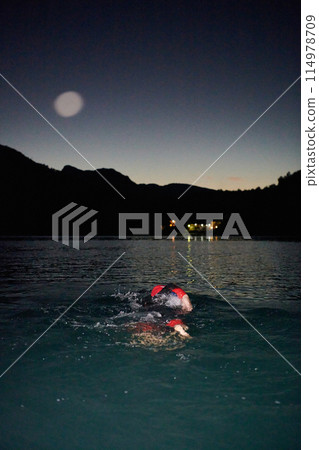 A determined professional triathlete undergoes rigorous night time training in cold waters, showcasing dedication and resilience in preparation for an upcoming triathlon swim competition 114978709