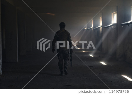A professional soldier in an abandoned building shows courage and determination in a war campaign 114978736