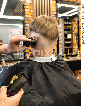 teenage boy with hairpins near barber combing his hair and holding hair clipper teenage boy with hairpins near barber combing his hair and holding hair clipper 114978828