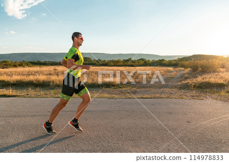 Triathlete in professional gear running early in the morning, preparing for a marathon, dedication to sport and readiness to take on the challenges of a marathon.  114978833