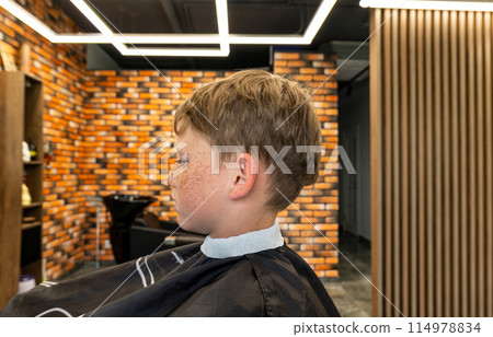 The picture of a small child before being cut was taken in a barbshop studio, the child has very beautiful blond hair that turns golden. The child is happy that he will have a new style of cutting. The picture of a small child before being cut was taken in a barbshop studio, the child has very beautiful blond hair that turns golden. The child is happy that he will have a new style of cutting. 114978834