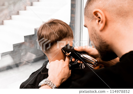 the process of hair styling a blond boy with with hair dryer and comb in a chair in a barbershop salon, a barbershop concept for men and boys 114978852