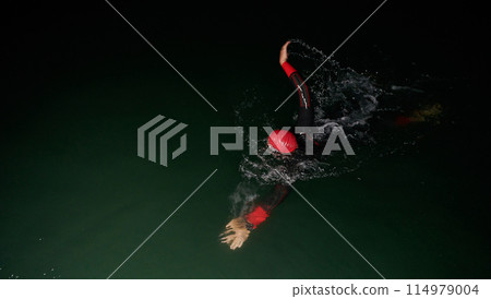 A determined professional triathlete undergoes rigorous night time training in cold waters, showcasing dedication and resilience in preparation for an upcoming triathlon swim competition A determined professional triathlete undergoes rigorous night time training in cold waters, showcasing dedication and resilience in preparation for an upcoming triathlon swim competition 114979004