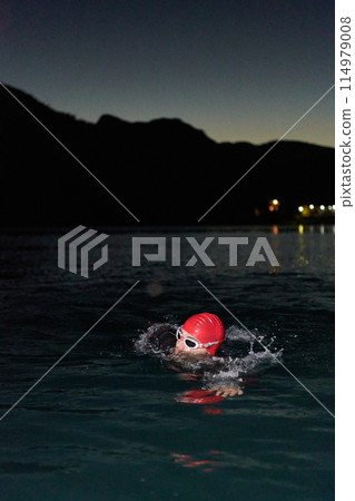 A determined professional triathlete undergoes rigorous night time training in cold waters, showcasing dedication and resilience in preparation for an upcoming triathlon swim competition A determined professional triathlete undergoes rigorous night time training in cold waters, showcasing dedication and resilience in preparation for an upcoming triathlon swim competition 114979008
