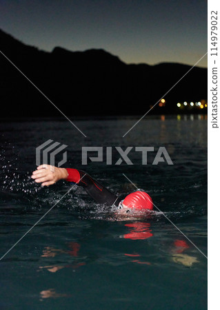 A determined professional triathlete undergoes rigorous night time training in cold waters, showcasing dedication and resilience in preparation for an upcoming triathlon swim competition 114979022