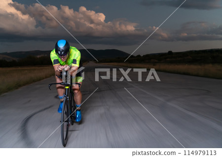 A triathlete rides his bike in the darkness of night, pushing himself to prepare for a marathon. The contrast between the darkness and the light of his bike creates a sense of drama and highlights the A triathlete rides his bike in the darkness of night, pushing himself to prepare for a marathon. The contrast between the darkness and the light of his bike creates a sense of drama and highlights the 114979113