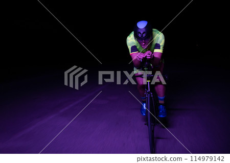 A triathlete rides his bike in the darkness of night, pushing himself to prepare for a marathon. The contrast between the darkness and the light of his bike creates a sense of drama and highlights the 114979142