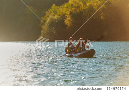 A young couple enjoying an idyllic kayak ride in the middle of a beautiful river surrounded by forest greenery in sunset time  114979154