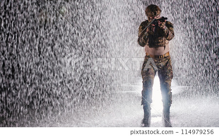 Army soldier in Combat Uniforms with an assault rifle, plate carrier and combat helmet going on a dangerous mission on a rainy night. 114979256