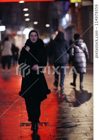 Muslim woman walking on an urban city street on a cold winter night wearing hijab 114979359