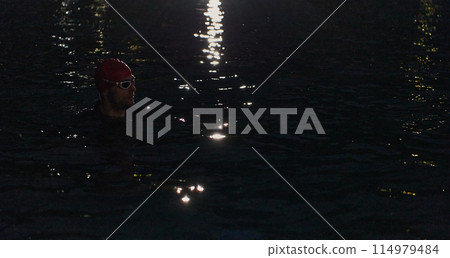A determined professional triathlete undergoes rigorous night time training in cold waters, showcasing dedication and resilience in preparation for an upcoming triathlon swim competition 114979484
