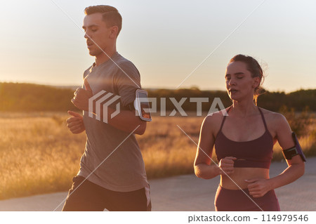 A handsome young couple running together during the early morning hours, with the mesmerizing sunrise casting a warm glow, symbolizing their shared love and vitality A handsome young couple running together during the early morning hours, with the mesmerizing sunrise casting a warm glow, symbolizing their shared love and vitality 114979546
