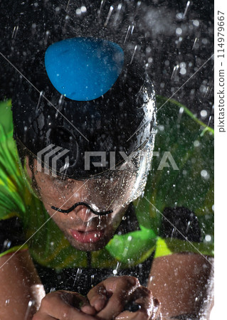 A triathlete braving the rain as he cycles through the night, preparing himself for the upcoming marathon. The blurred raindrops in the foreground and the dark, moody atmosphere in the background add 114979667