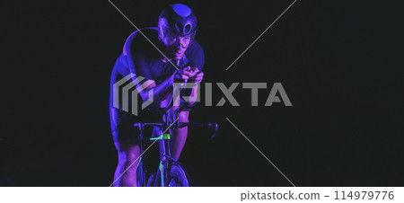 A triathlete rides his bike in the darkness of night, pushing himself to prepare for a marathon. The contrast between the darkness and the light of his bike creates a sense of drama and highlights the A triathlete rides his bike in the darkness of night, pushing himself to prepare for a marathon. The contrast between the darkness and the light of his bike creates a sense of drama and highlights the 114979776