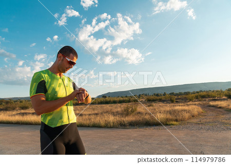The triathlete checking his training statistics on a smartwatch, analyzing his performance and progress. With dedication, discipline, and perseverance, he strives to improve his physical abilities and 114979786