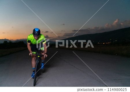 A triathlete rides his bike in the darkness of night, pushing himself to prepare for a marathon. The contrast between the darkness and the light of his bike creates a sense of drama and highlights the 114980025