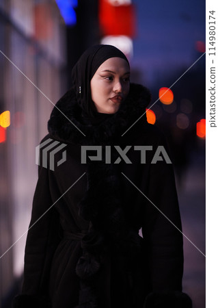 Muslim woman walking on an urban city street on a cold winter night wearing hijab 114980174