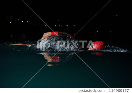 A determined professional triathlete undergoes rigorous night time training in cold waters, showcasing dedication and resilience in preparation for an upcoming triathlon swim competition A determined professional triathlete undergoes rigorous night time training in cold waters, showcasing dedication and resilience in preparation for an upcoming triathlon swim competition 114980177
