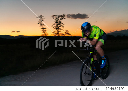 A triathlete rides his bike in the darkness of night, pushing himself to prepare for a marathon. The contrast between the darkness and the light of his bike creates a sense of drama and highlights the A triathlete rides his bike in the darkness of night, pushing himself to prepare for a marathon. The contrast between the darkness and the light of his bike creates a sense of drama and highlights the 114980191