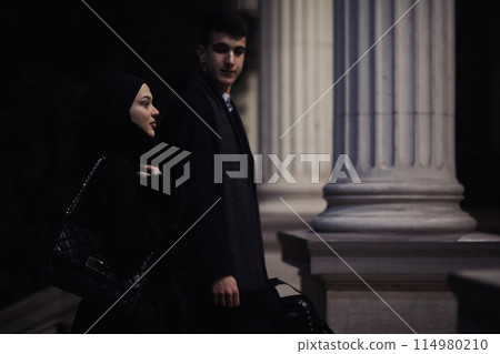 Happy multicultural business couple walking together outdoors in an urban city street at night near a jewelry shopping store window. Happy multicultural business couple walking together outdoors in an urban city street at night near a jewelry shopping store window. 114980210