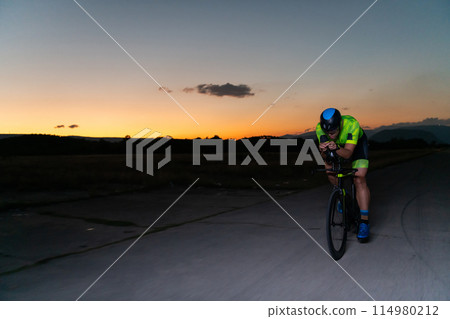 A triathlete rides his bike in the darkness of night, pushing himself to prepare for a marathon. The contrast between the darkness and the light of his bike creates a sense of drama and highlights the A triathlete rides his bike in the darkness of night, pushing himself to prepare for a marathon. The contrast between the darkness and the light of his bike creates a sense of drama and highlights the 114980212
