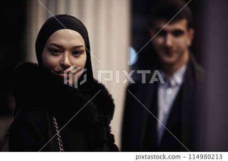 Happy multicultural business couple walking together outdoors in an urban city street at night near a jewelry shopping store window. Happy multicultural business couple walking together outdoors in an urban city street at night near a jewelry shopping store window. 114980213