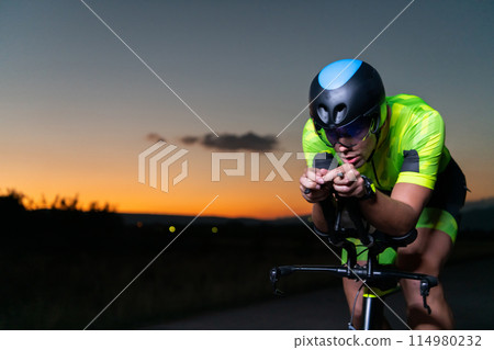 A triathlete rides his bike in the darkness of night, pushing himself to prepare for a marathon. The contrast between the darkness and the light of his bike creates a sense of drama and highlights the A triathlete rides his bike in the darkness of night, pushing himself to prepare for a marathon. The contrast between the darkness and the light of his bike creates a sense of drama and highlights the 114980232