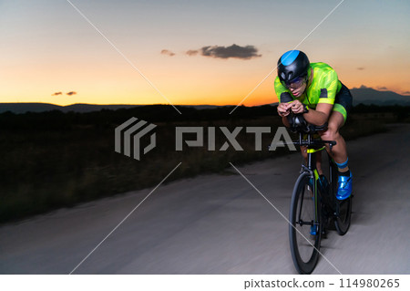 A triathlete rides his bike in the darkness of night, pushing himself to prepare for a marathon. The contrast between the darkness and the light of his bike creates a sense of drama and highlights the A triathlete rides his bike in the darkness of night, pushing himself to prepare for a marathon. The contrast between the darkness and the light of his bike creates a sense of drama and highlights the 114980265