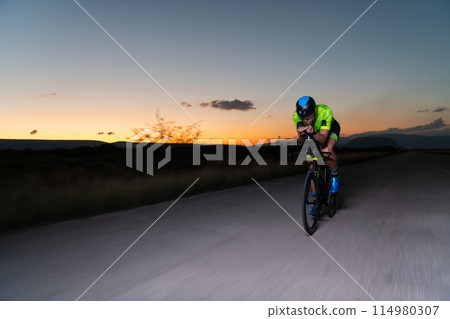 A triathlete rides his bike in the darkness of night, pushing himself to prepare for a marathon. The contrast between the darkness and the light of his bike creates a sense of drama and highlights the A triathlete rides his bike in the darkness of night, pushing himself to prepare for a marathon. The contrast between the darkness and the light of his bike creates a sense of drama and highlights the 114980307