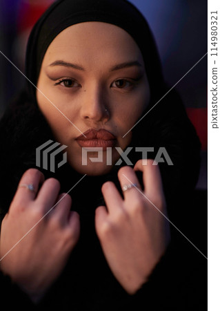 Muslim woman walking on an urban city street on a cold winter night wearing hijab Muslim woman walking on an urban city street on a cold winter night wearing hijab 114980321