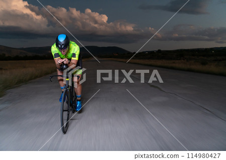 A triathlete rides his bike in the darkness of night, pushing himself to prepare for a marathon. The contrast between the darkness and the light of his bike creates a sense of drama and highlights the A triathlete rides his bike in the darkness of night, pushing himself to prepare for a marathon. The contrast between the darkness and the light of his bike creates a sense of drama and highlights the 114980427