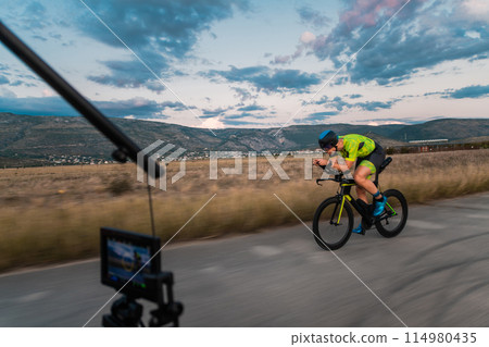 A videographer recording a triathlete riding his bike preparing for an upcoming marathon.Athlete's physical endurance and the dedication required to succeed in the sport. 114980435