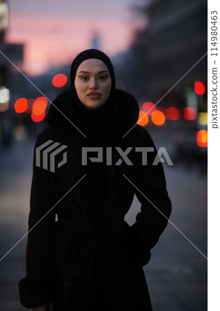 Muslim woman walking on an urban city street on a cold winter night wearing hijab 114980463